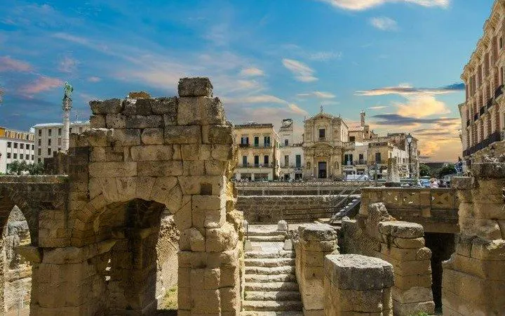 Ancient Roman amphitheater ruins in Lecce with historic buildings in the background.