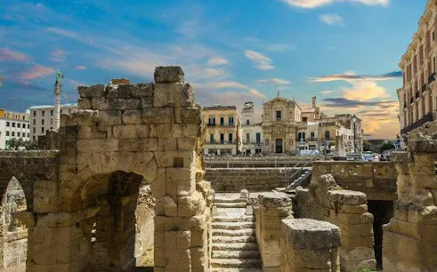 Ancient Roman amphitheater ruins in Lecce with historic buildings in the background.