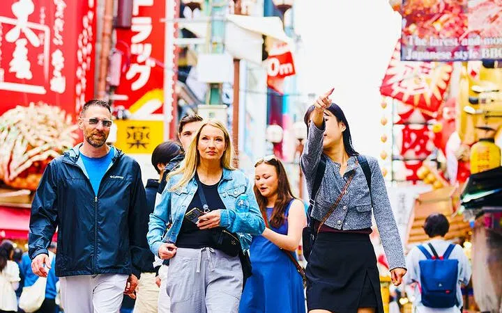 Tourists exploring vibrant Osaka backstreets with colorful signs and local street food stalls.