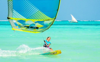 Kitesurfer gliding over turquoise waters in Zanzibar, Tanzania, with a traditional dhow in the background.