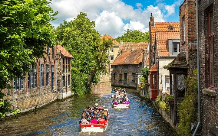Boat tour on a canal in Bruges, passing historic brick buildings and lush greenery.