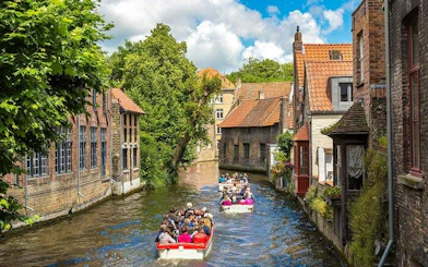 Boat tour on a canal in Bruges, passing historic brick buildings and lush greenery.