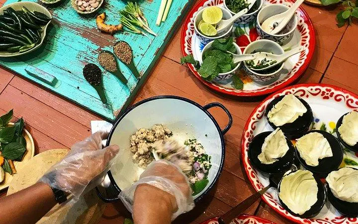 Hands preparing ingredients at Silom Thai Cooking School, Bangkok, with herbs and spices on a table.