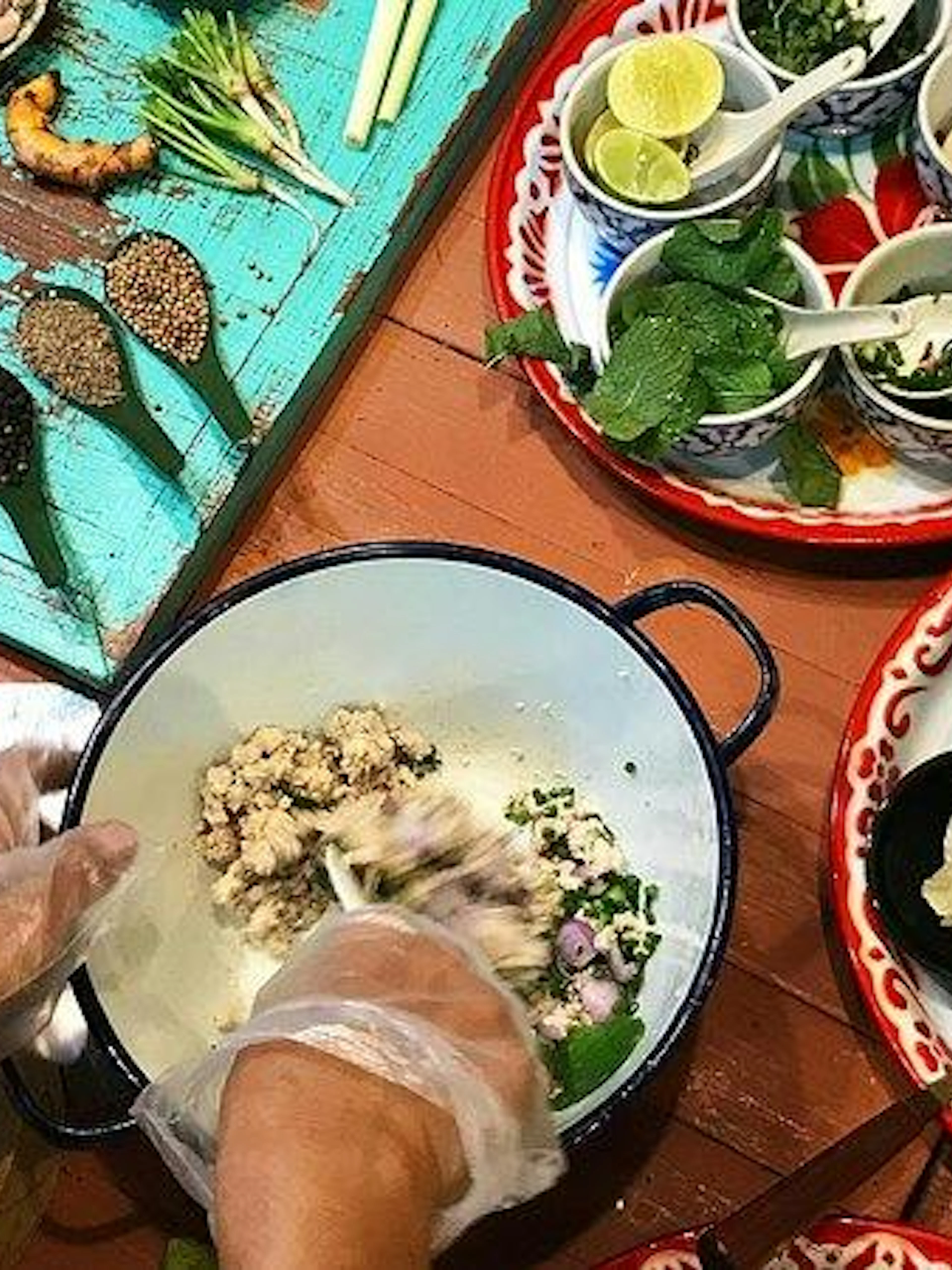 Hands preparing ingredients at Silom Thai Cooking School, Bangkok, with herbs and spices on a table.