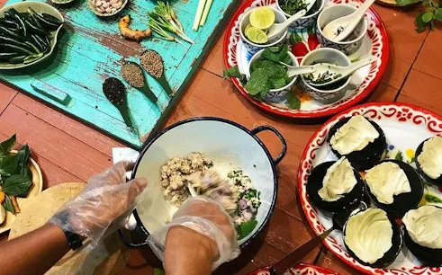 Hands preparing ingredients at Silom Thai Cooking School, Bangkok, with herbs and spices on a table.