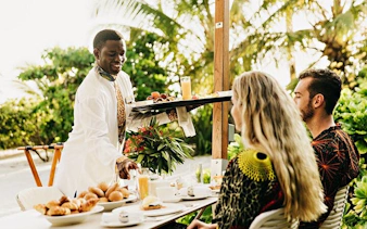 Server bringing breakfast to couple at outdoor table in Zanzibar.