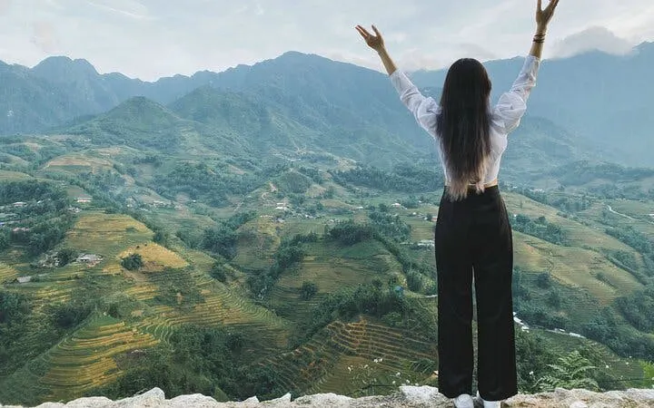 Person overlooking Sapa rice terraces and mountains during trekking tour in Vietnam.