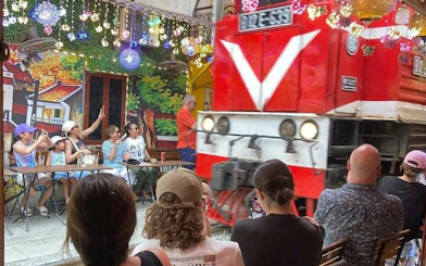 Motorbike tour group watches train pass through Hanoi street cafe.