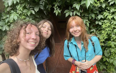 Three people smiling in front of a vine-covered doorway in Budapest.