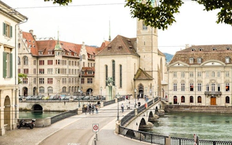 Zurich cityscape with Grossmünster church and Limmat River bridge, part of self-guided exploration game.