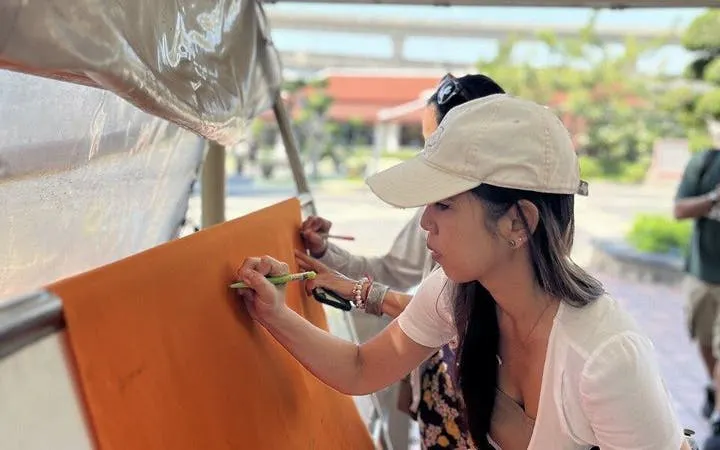 Woman writing on orange fabric at Erawan Museum during Bangkok day trip.