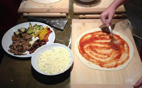 Pizza dough with tomato sauce being prepared in a Naples cooking class.