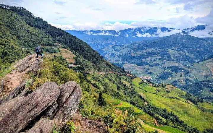 Hiker on a rocky path overlooking terraced rice fields and mountains in Sapa, Vietnam.
