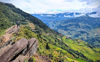 Hiker on a rocky path overlooking terraced rice fields and mountains in Sapa, Vietnam.