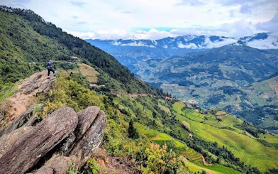 Hiker on a rocky path overlooking terraced rice fields and mountains in Sapa, Vietnam.