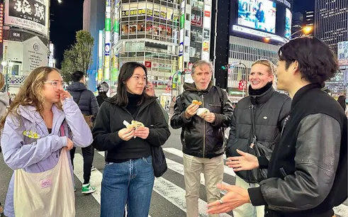 Group enjoying Shibuya walking tour at night, Tokyo, with guide sharing insights.
