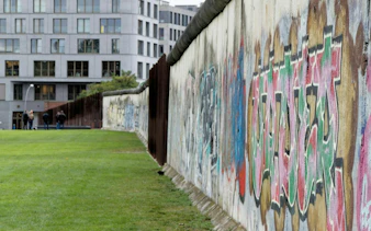 Berlin Wall with graffiti at Bernauer Strasse, part of the Berlin Wall Memorial, with people walking nearby.