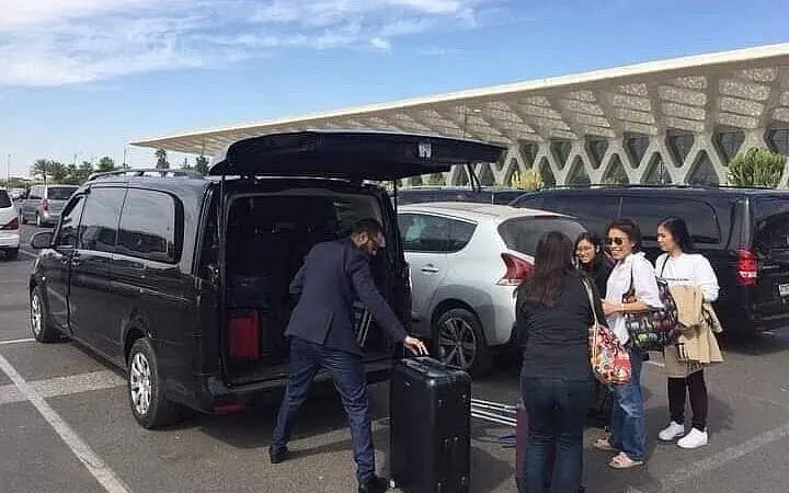 Private transfer service with passengers loading luggage at Marrakesh airport.