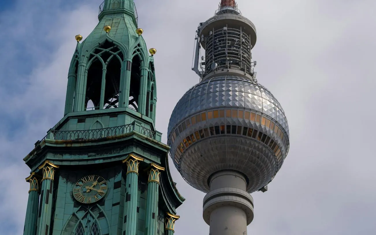 Berlin TV Tower and St. Mary's Church spire against cloudy sky.