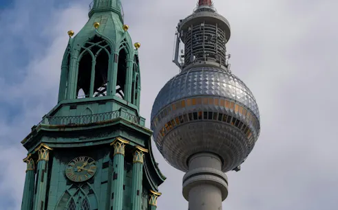 Berlin TV Tower and St. Mary's Church spire against cloudy sky.