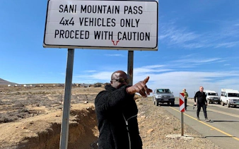 Sani Pass sign with 4x4 vehicles on road, Lesotho tour from Durban.