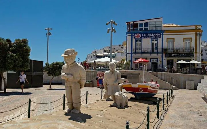 Stone sculptures of a fisherman and woman with a dog in Albufeira town square, Portugal.
