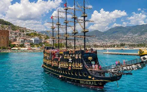 Pirate ship sailing near Alanya coast with tourists on deck, mountains in background.