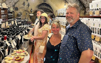 Tourists enjoying wine tasting in a cellar in Montepulciano, Italy, surrounded by bottles and local delicacies.