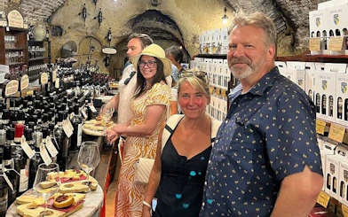 Tourists enjoying wine tasting in a cellar in Montepulciano, Italy, surrounded by bottles and local delicacies.