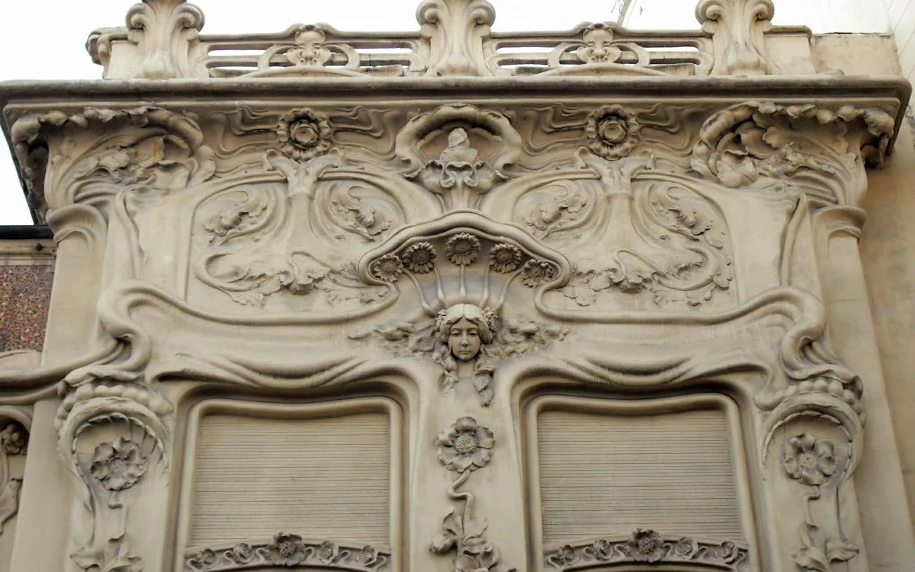 Facade detail of Art Nouveau architecture in Malasaña, Madrid, featuring ornate floral and face motifs.