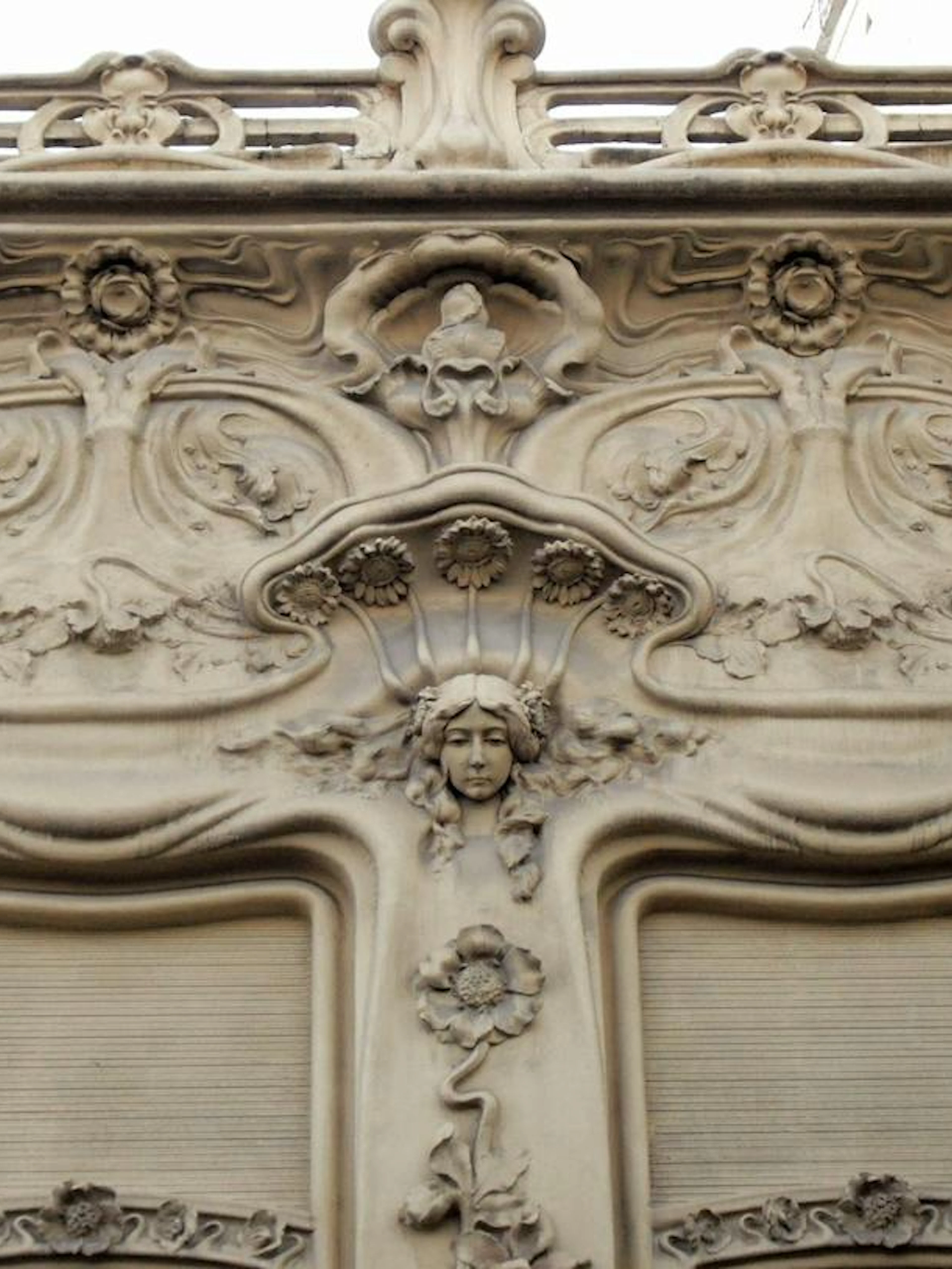 Facade detail of Art Nouveau architecture in Malasaña, Madrid, featuring ornate floral and face motifs.