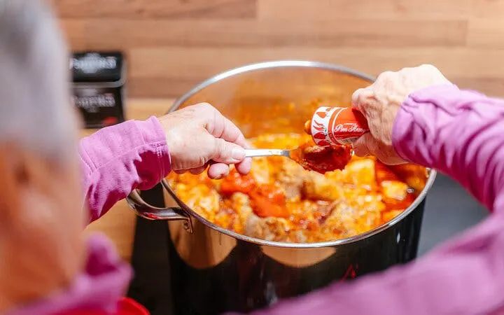 Person adding paprika to a pot of traditional Hungarian stew during a cooking class in Budapest.