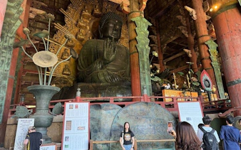 Giant Buddha statue inside Todai-ji Temple, Nara, with visitors exploring the historic site.