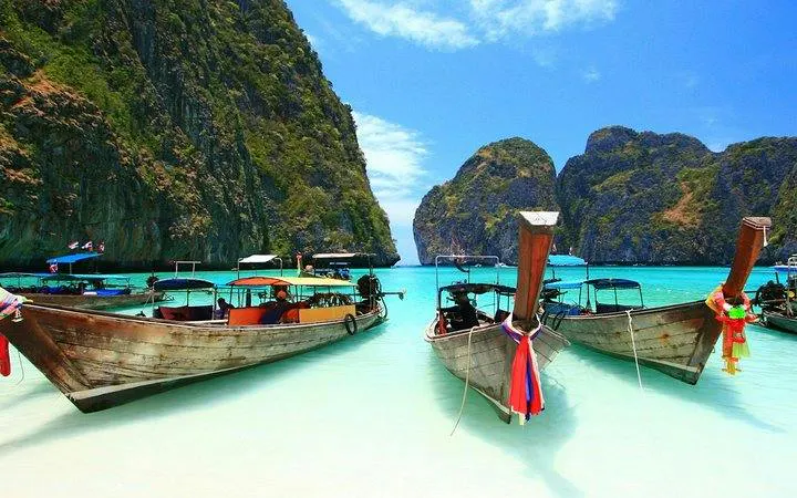 Longtail boats anchored at Banana Beach, Koh Hey, with clear turquoise water and lush cliffs, Phuket.