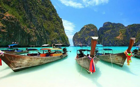 Longtail boats anchored at Banana Beach, Koh Hey, with clear turquoise water and lush cliffs, Phuket.