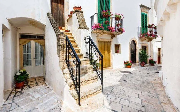 Stone staircase and flower-adorned balconies in a quaint alleyway, Valle d'Itria, Italy.