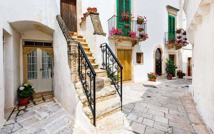 Stone staircase and flower-adorned balconies in a quaint alleyway, Valle d'Itria, Italy.