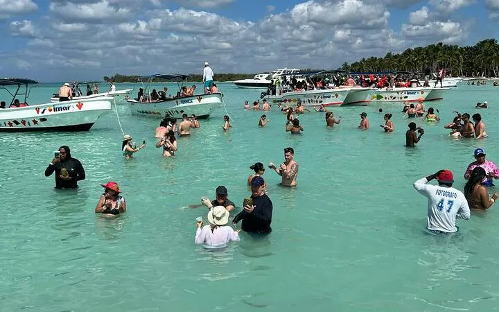 Tourists enjoying the water near boats on Saona Island, Punta Cana, during a day trip with beachside lunch.