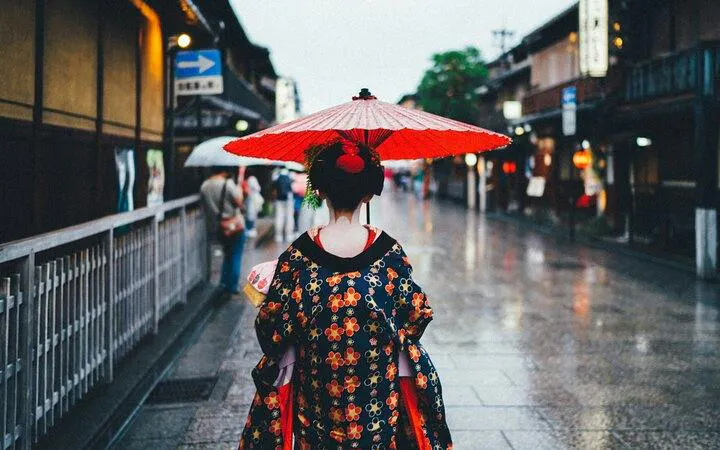 Geisha with red umbrella walking in Gion district, Kyoto.