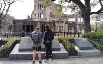 Two visitors observe the Hiroshima Atomic Bomb Dome during a guided tour.