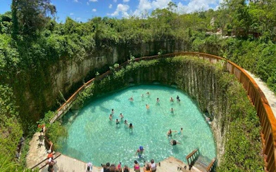 Visitors swimming in a blue lagoon cenote surrounded by lush greenery in Punta Cana.