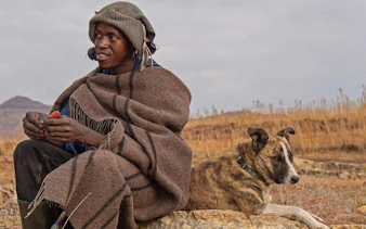 Man in traditional attire with a dog in Lesotho landscape during Sani Pass tour.