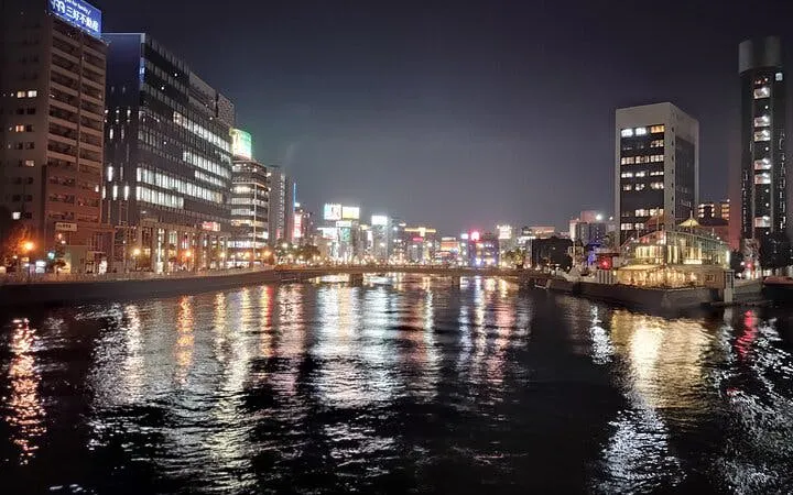 Nakasu riverfront at night with illuminated buildings, Fukuoka food stall tour.