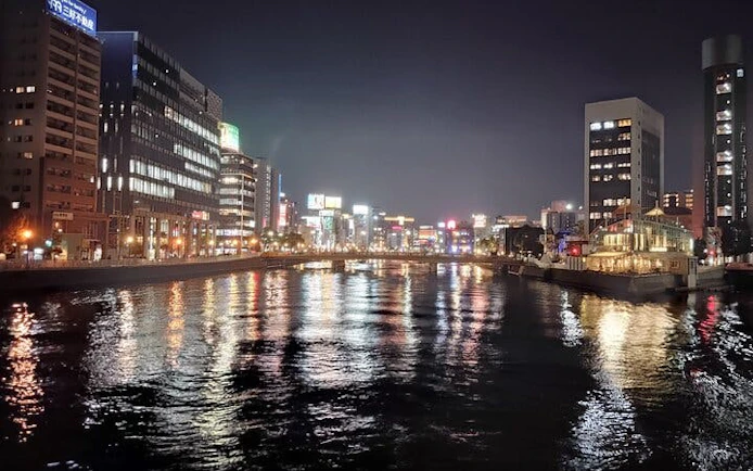 Nakasu riverfront at night with illuminated buildings, Fukuoka food stall tour.