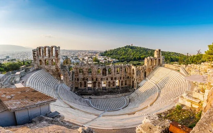Ancient amphitheater in Athens with cityscape and hill in the background.