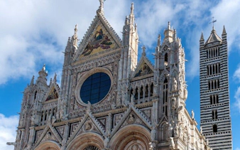 Siena Cathedral facade and bell tower under a blue sky.