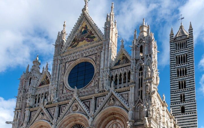 Siena Cathedral facade and bell tower under a blue sky.