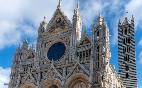 Siena Cathedral facade and bell tower under a blue sky.