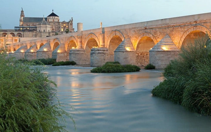 Roman Bridge of Cordoba illuminated at dusk with the Mezquita in the background.