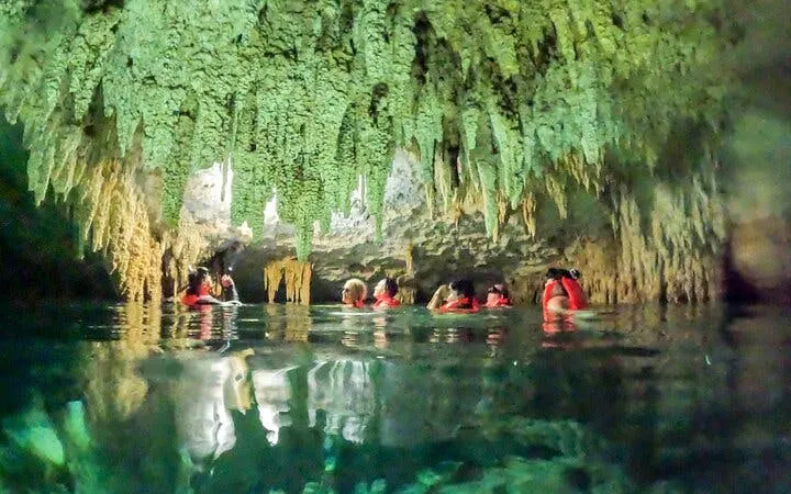 Small group swimming in a cenote cave with stalactites, guided tour in Akumal, Mexico.